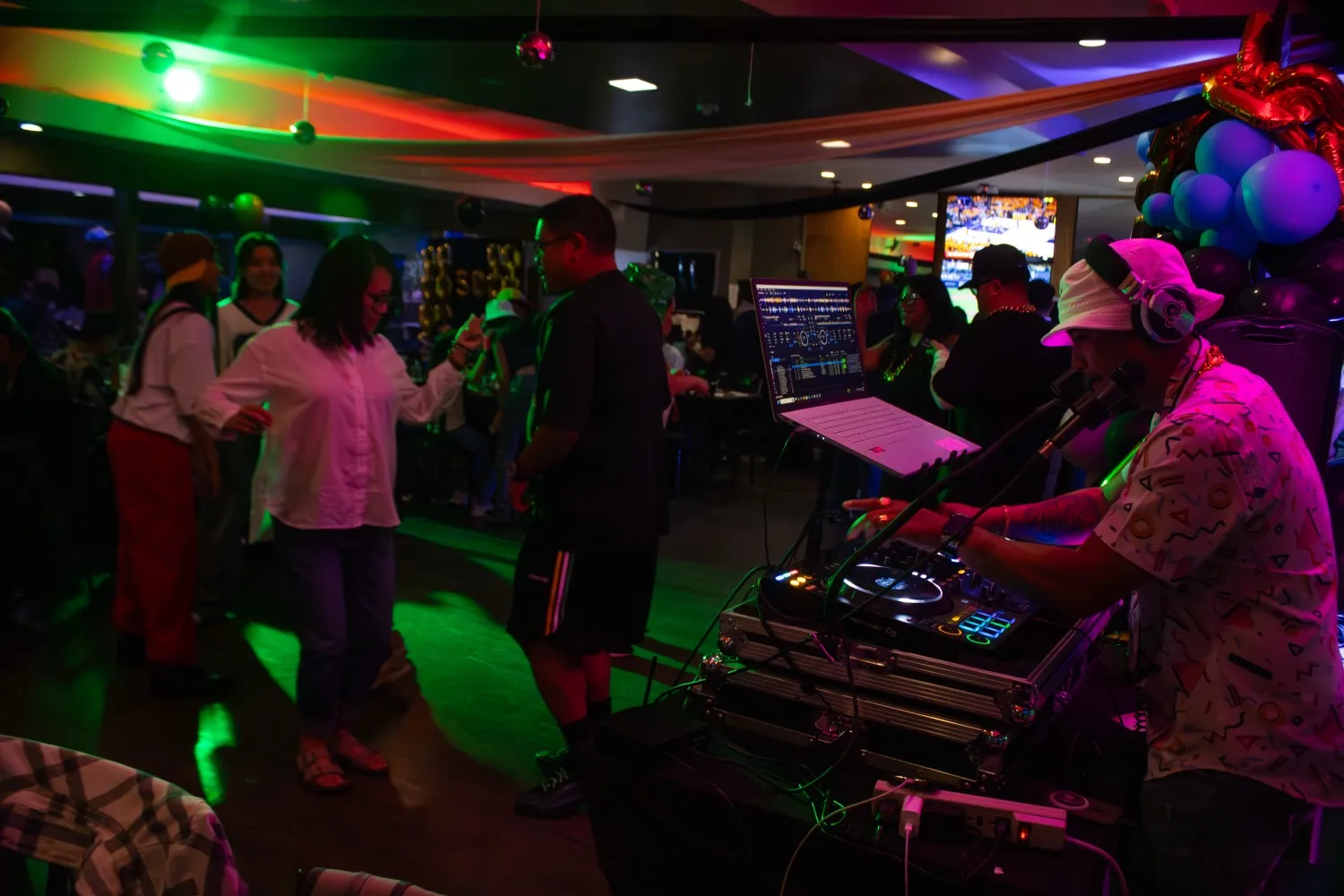 Packed dancefloor with the DJ mixing under colored lights